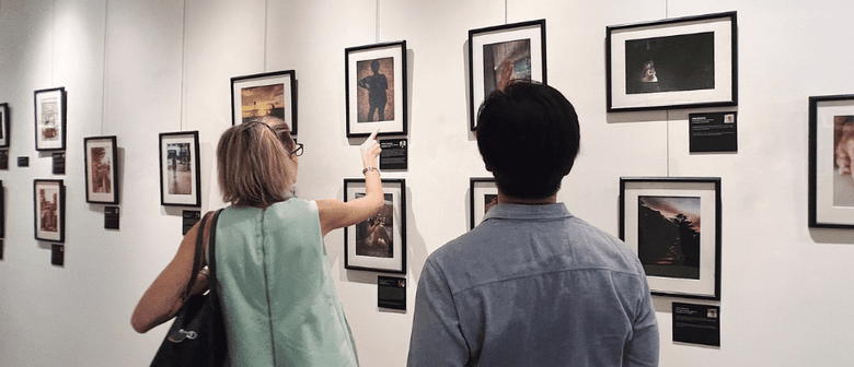 A man and a woman at a photography exhibition in a gallery, looking at photos displayed on the wall. The woman is pointing to a specific photo.